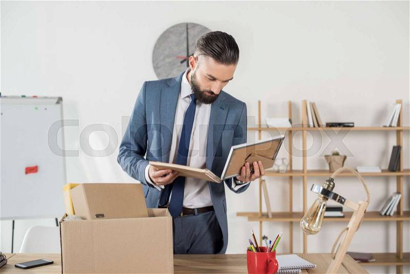 Portrait of fired upset businessman looking at photos at workplace in office, stock photo