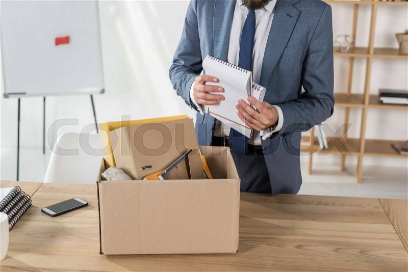 Cropped shot of fired businessman packing office supplies in cardboard box at workplace, stock photo