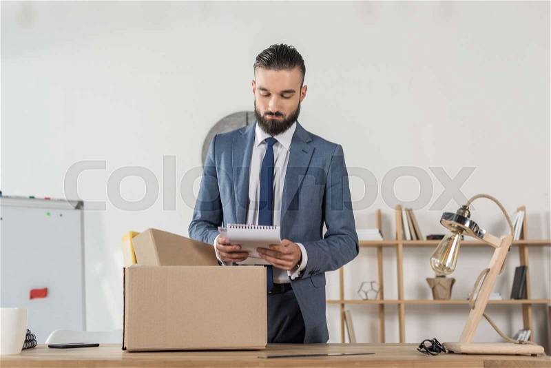 Portrait of fired sad businessman packing office supplies at workplace, stock photo
