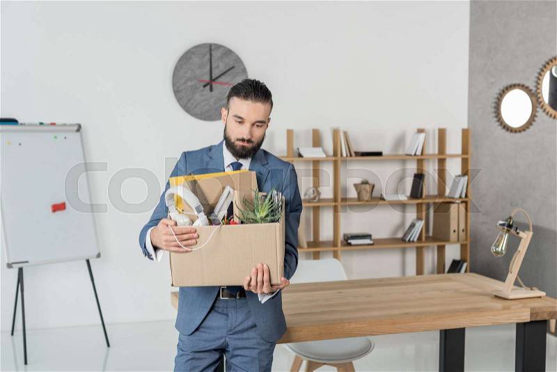 Portrait of fired sad businessman with cardboard box in hands standing at workplace in office, stock photo