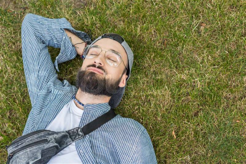 Overhead view of smiling man with eyes closed lying on grass, stock photo