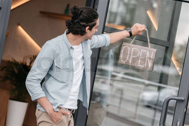 Young boutique owner hanging open sign on the door of his shop, stock photo