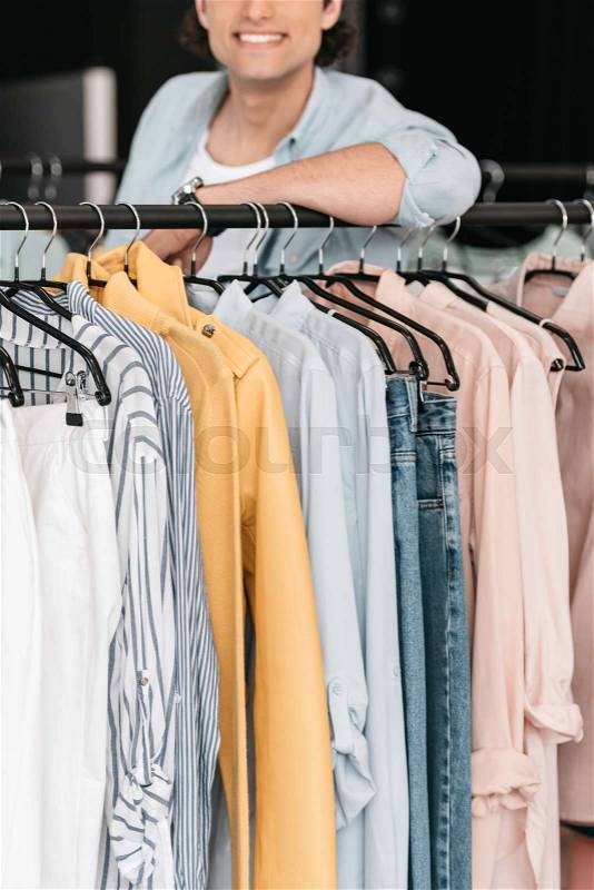 Cropped shot of young smiling boutique owner standing near clothes, stock photo