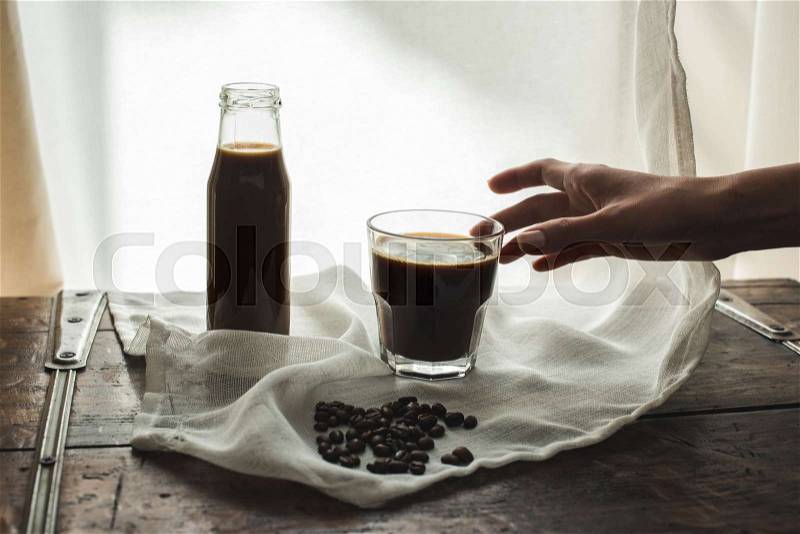 Person taking glass of coffee from cloth with roasted coffee beans, stock photo