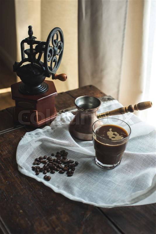 Vintage hand mill, turkish coffee pot with glass of coffee on white cloth with coffee beans, stock photo