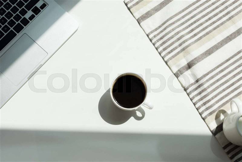 White working desk with laptop computer and cup of black coffee and tablecloth, stock photo