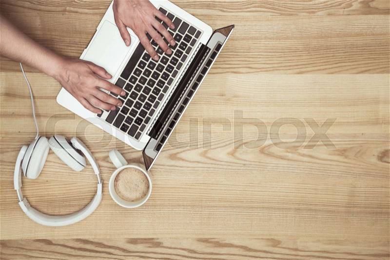 Top view of man typing on laptop on wooden tabletop with headphones and coffee cup , stock photo