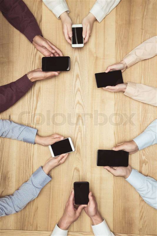Top view of businesspeople on meeting with smartphones with blank screens on wooden tabletop, stock photo