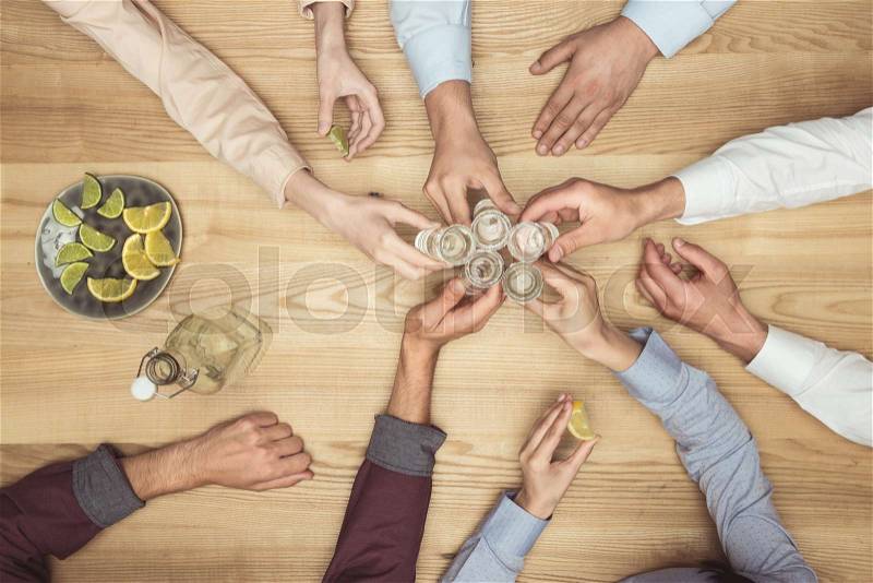 Top view of friends hands with tequila shots on wooden tabletop , stock photo