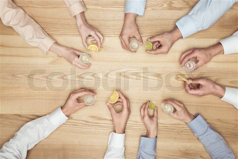 Top view of friends hands with tequila shots on wooden tabletop , stock photo