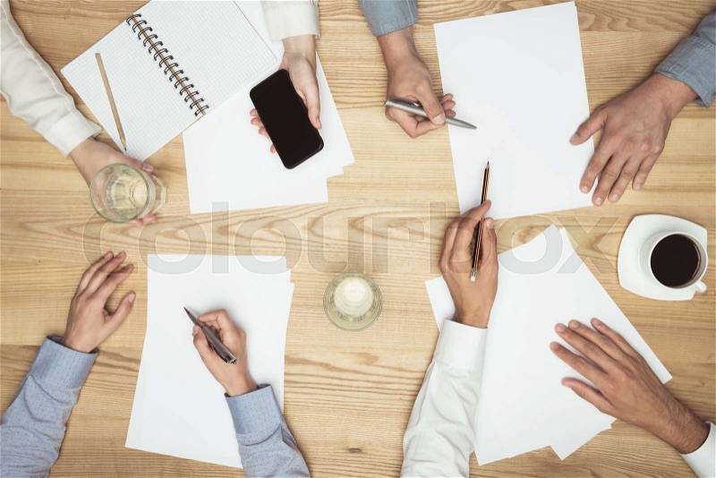 Top view of businesspeople on meeting with documents and smartphone at workplace, stock photo