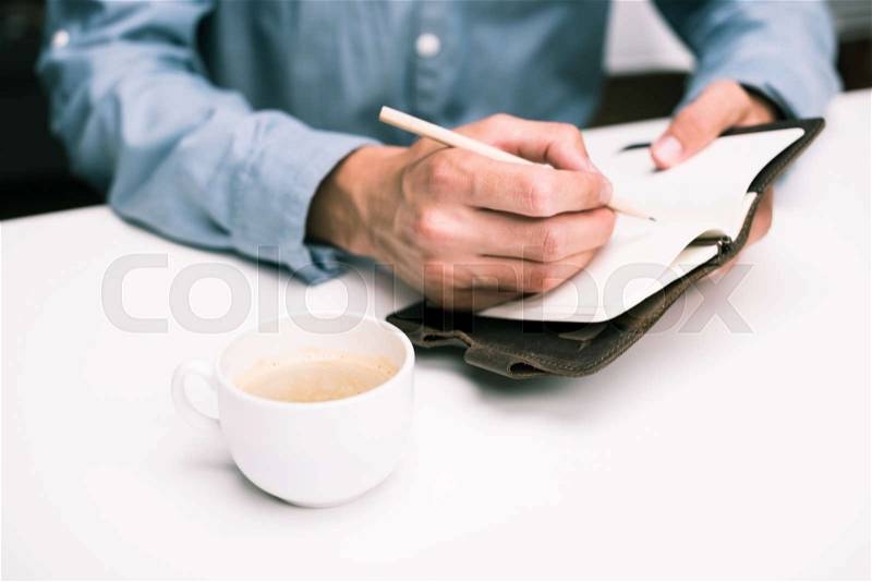 Cropped view of male hands with coffee cup writing in diary , stock photo