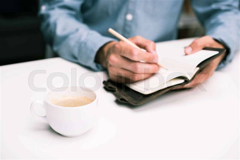 Cropped view of male hands with coffee cup writing in diary, stock photo