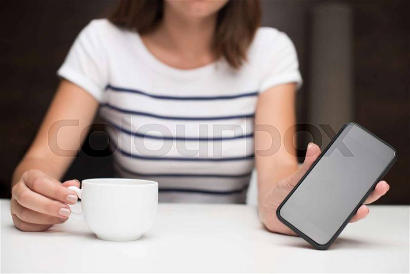 Cropped view of woman with coffee cup holding smartphone with blank screen, stock photo
