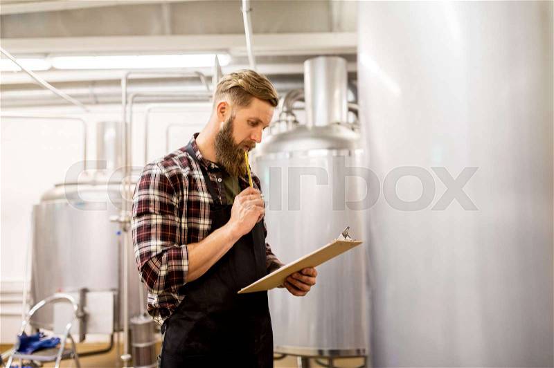 Manufacture, business and people concept - man with clipboard working at craft brewery or beer plant, stock photo