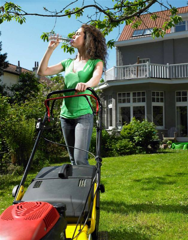 Woman mowing lawn in the sun, stock photo