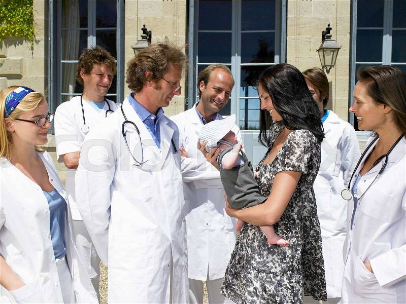Woman holding her baby, doctors around, stock photo