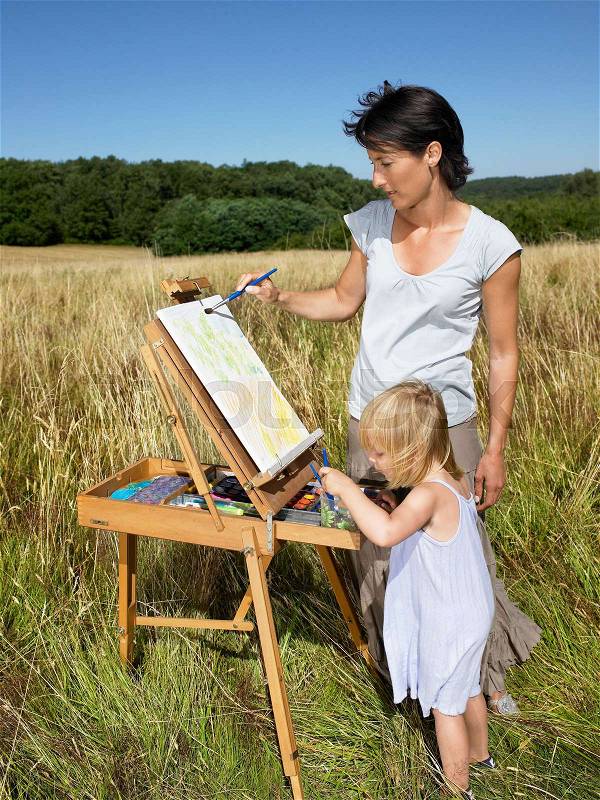 Mother and daughter painting in a field, stock photo