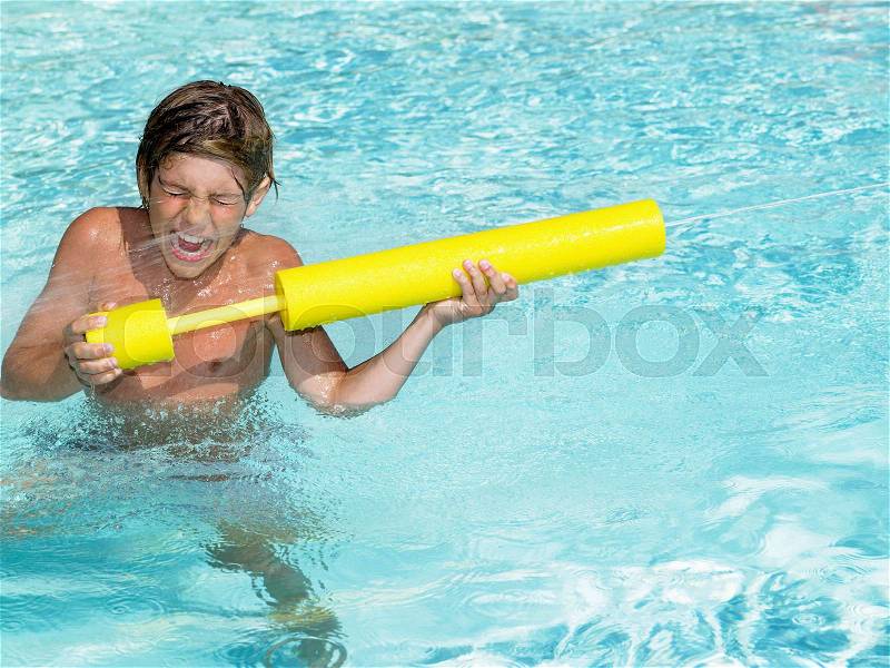 Boy playing with water gun in pool, stock photo