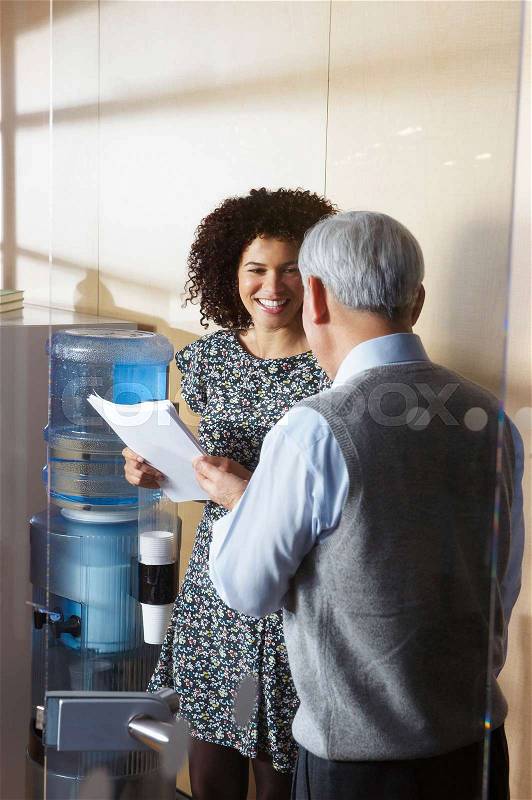 Co-workers by office water cooler, stock photo