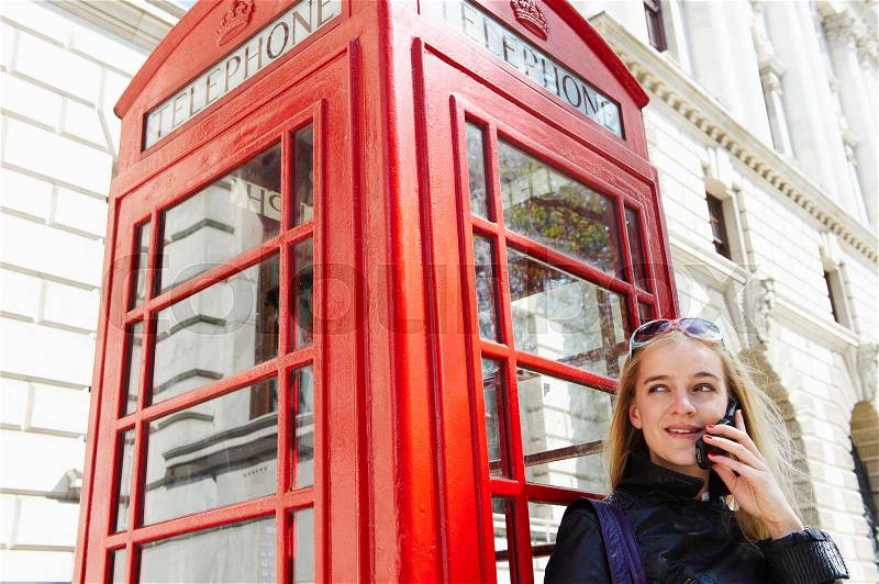 Woman next to phone booth, on her cell, stock photo