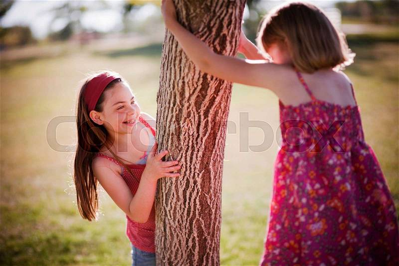 2 young girls playing around tree, stock photo