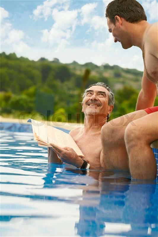 Older man reading news in swimming pool, stock photo