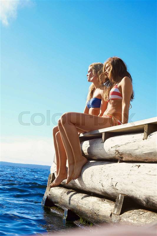 Teenage girls dangling legs over pier, stock photo