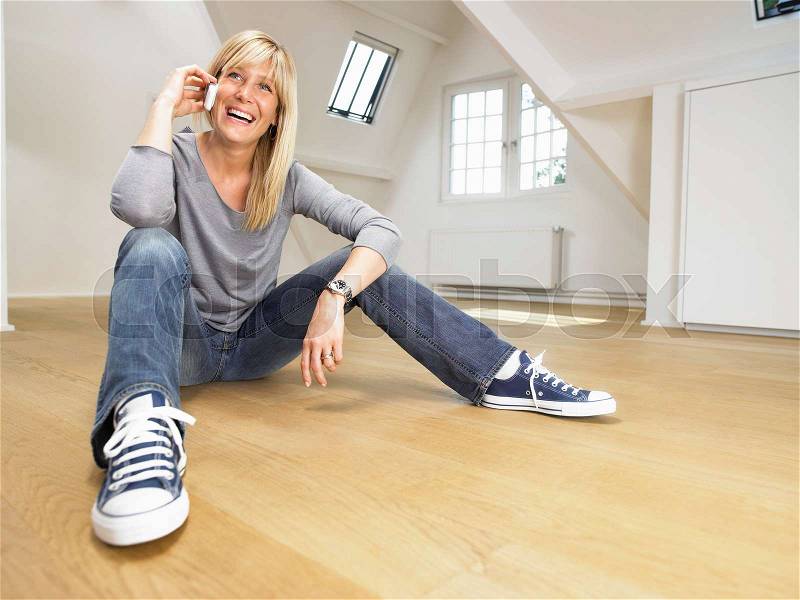 Happy woman seated on wooden floor, stock photo