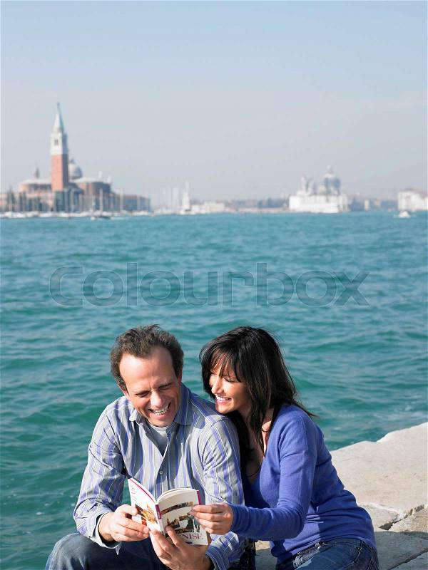 Couple sitting looking at guide book, stock photo