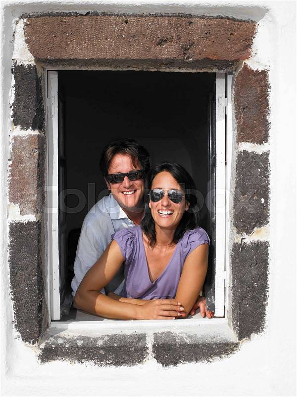 Couple looking through window, smiling, stock photo