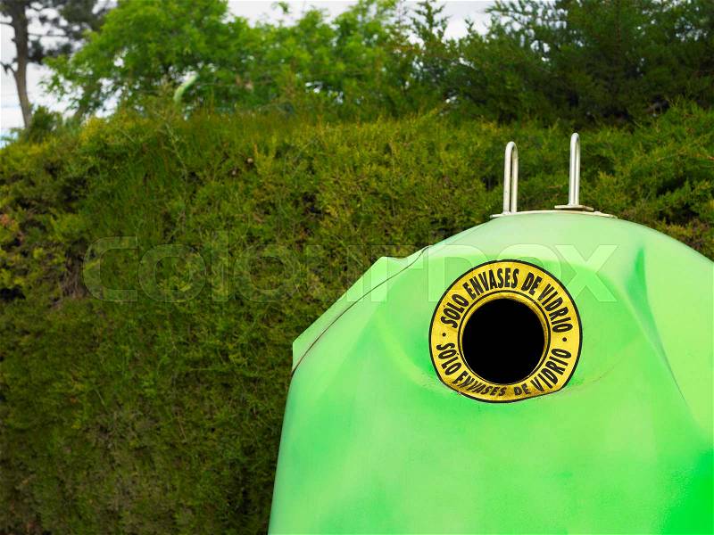 Green recycling bin by hedge, stock photo