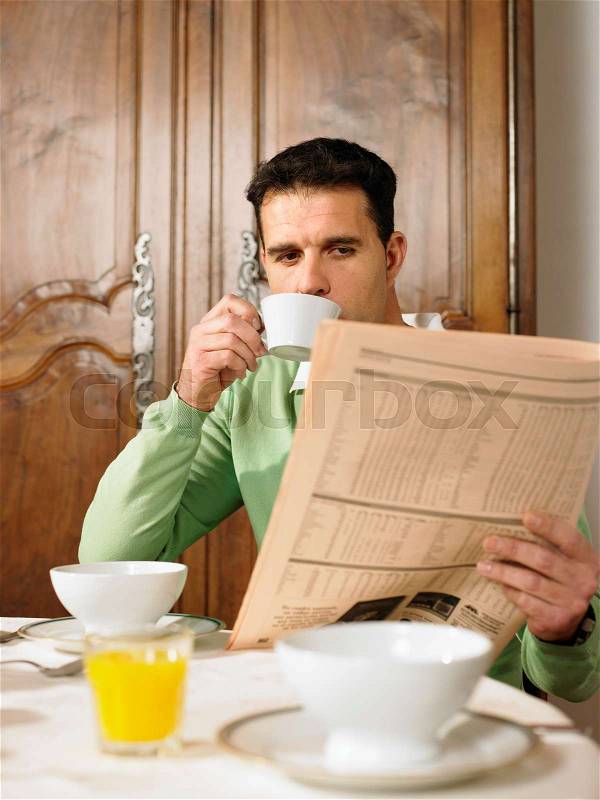 Man reading paper at breakfast table, stock photo
