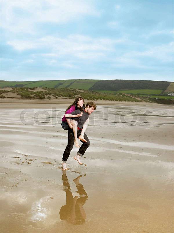 Man carrying woman piggy back on beach, stock photo