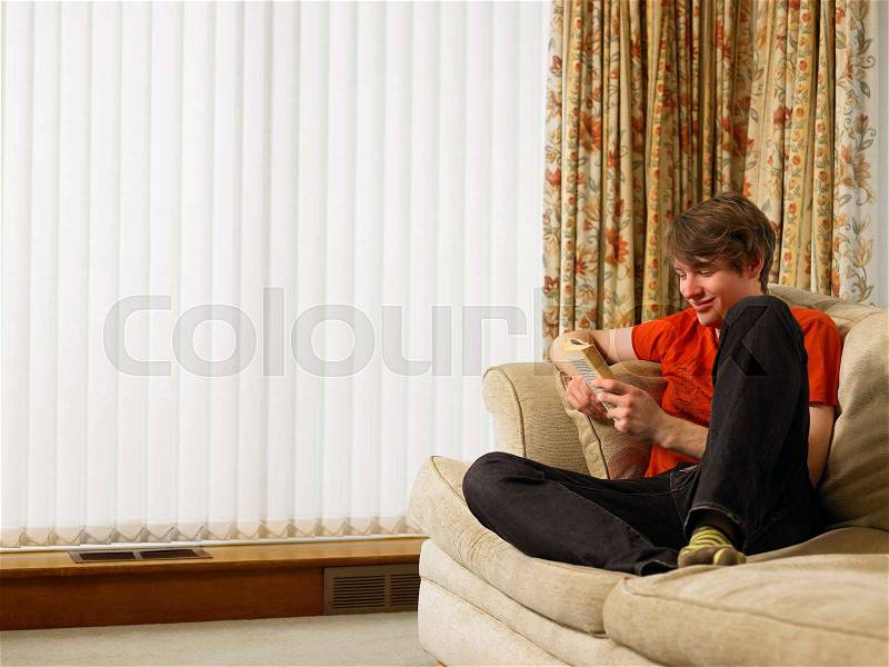 Young man relaxing on sofa reading book, stock photo
