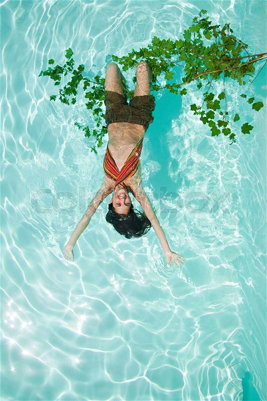 Woman hanging upside down from branch in pool, stock photo