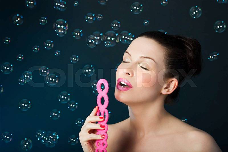 Young brunette woman blowing bubbles with bubble wand, stock photo
