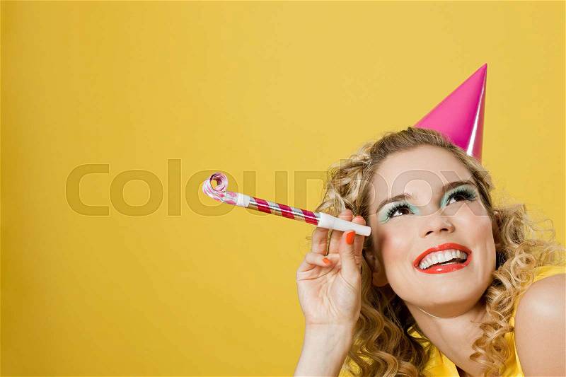 Young woman wearing party hat with party blower, stock photo