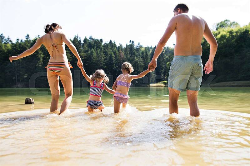 Young mother and father with their little daughters in the the lake. Summer heat and water. Rear view, stock photo