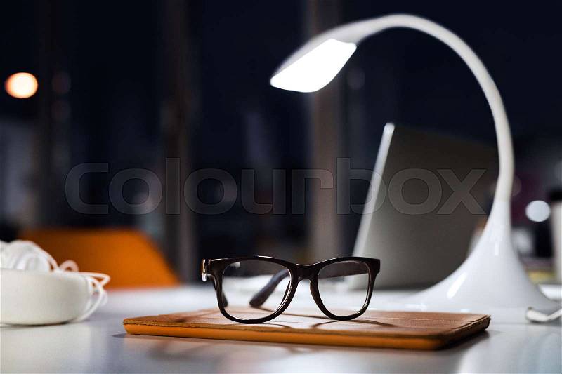 Office desk at night with eyeglasses, lamp and tablet. The interior of working office space, stock photo