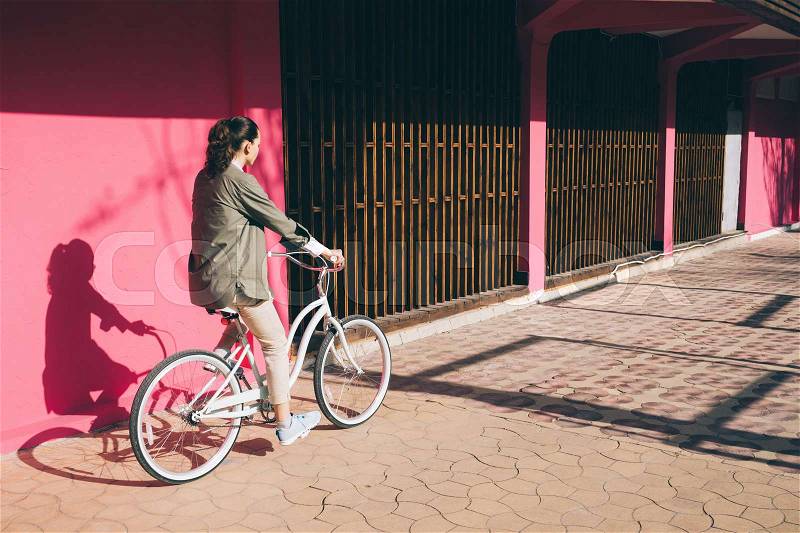 Woman in a jacket rides a city bike against the background of a pink wall, stock photo