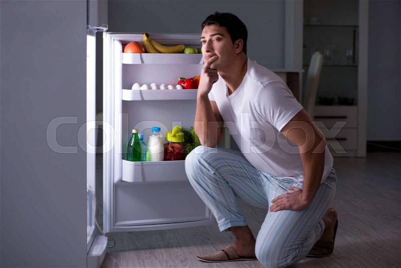 Man at the fridge eating at night, stock photo