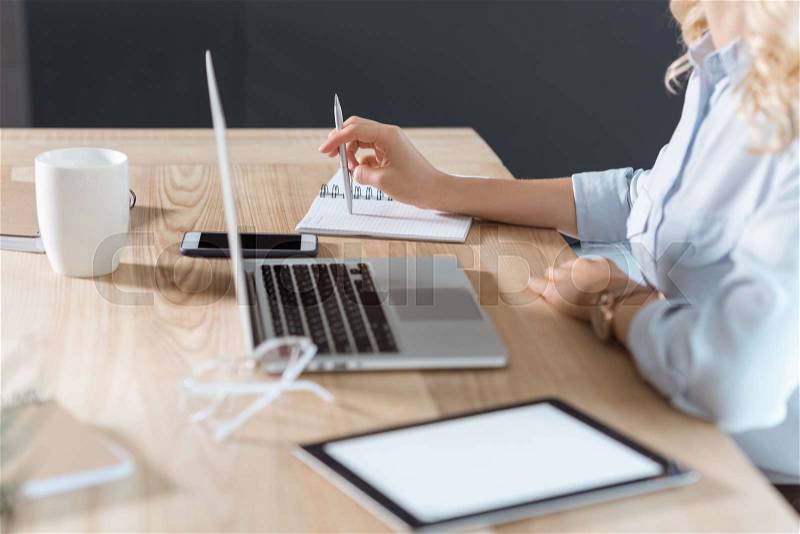 Cropped shot of businesswoman working at workplace with digital devices and notebooks in office, stock photo
