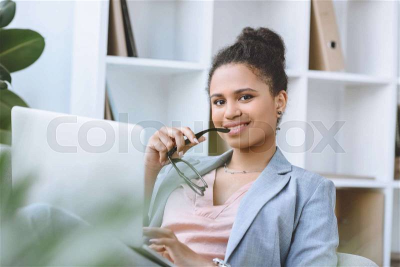 Portrait of smiling african american businesswoman with laptop looking at camera, stock photo