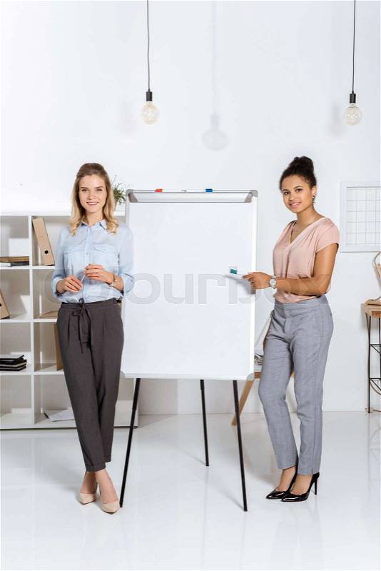 Smiling african american businesswoman pointing at white board with colleague standing near by, stock photo