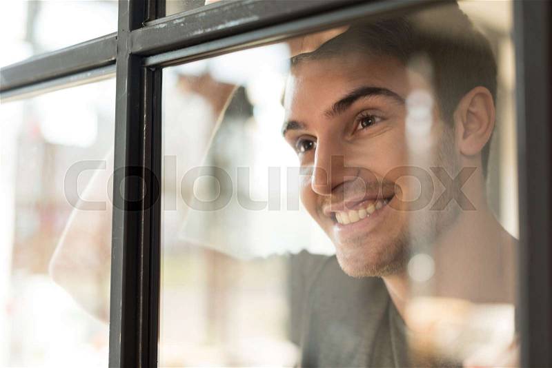 Portrait of smiling caucasian man looking away through glass door, stock photo