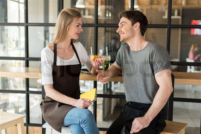 Young waiter and waitress having conversation during break at work in cafe, stock photo