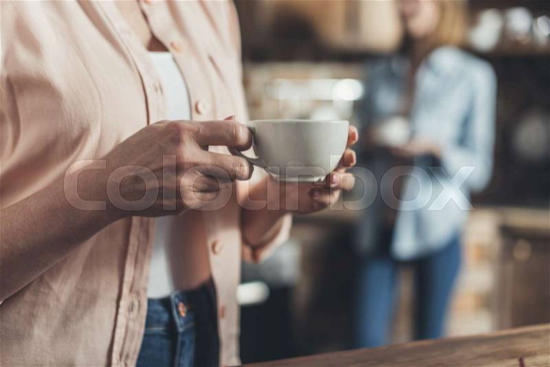 Cropped image, middle section of person holding coffee cup, standing in kitchen, stock photo