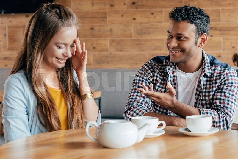 Smiling young man talking to shy woman sitting in cafe, stock photo