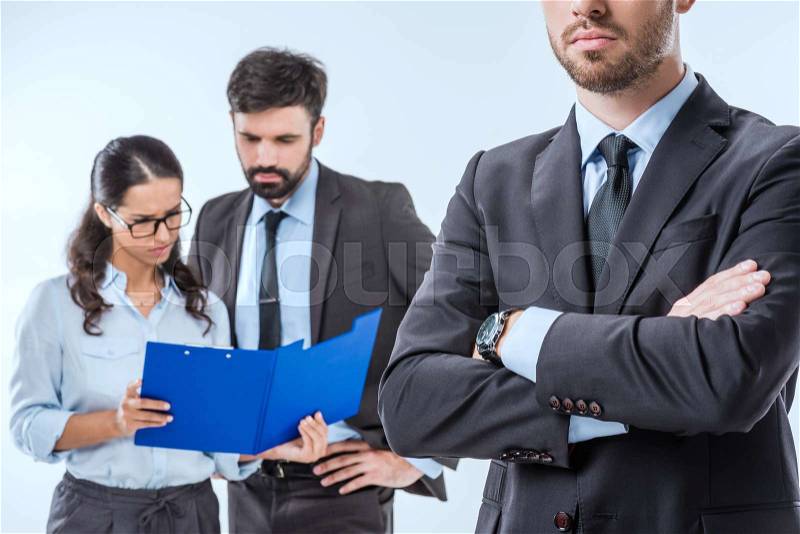 Cropped shot of businessman with arms crossed and colleagues discussing work behind , stock photo